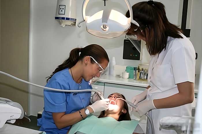 Odontóloga y asistente realizando un tratamiento dental a una paciente en un gabinete clínico.